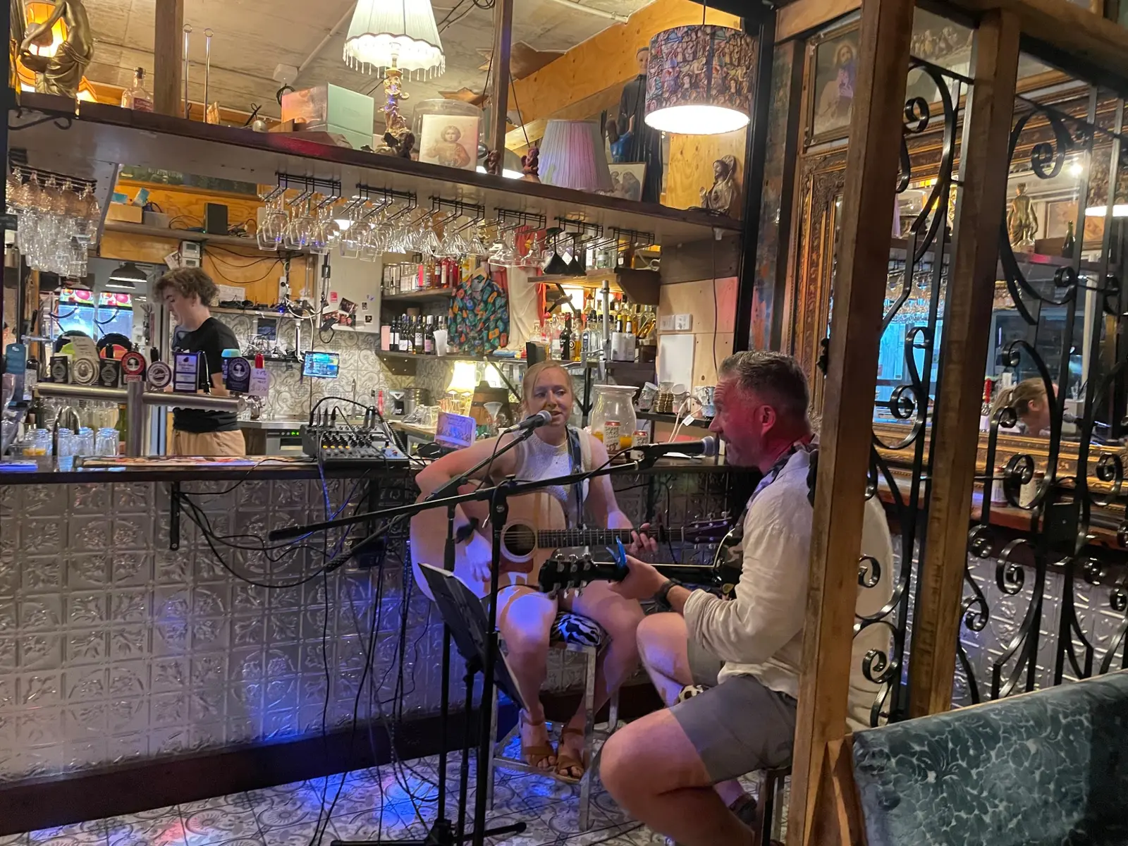 The duo singing and playing acoustic guitars beside a bar